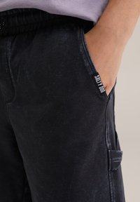 Čierne tepláky s jemne vyblednutou textúrou, vybavené elastickým pásom a bočnou kapsou, označené štítkom "SALTY DOG".