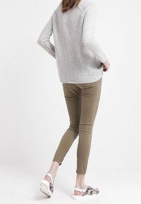 Ljusgrå stickad tröja, olivgröna tajta byxor och mönstrade sandaler. Outfiten har en avslappnad passform och textil med struktur.