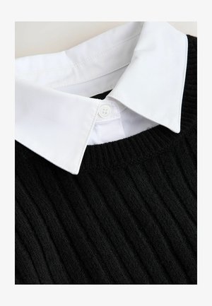 Svart ribbad stickad tröja med en vit skjortkrage. Tyget har en mjuk textur och kragen är detaljerad med en enda knapp.