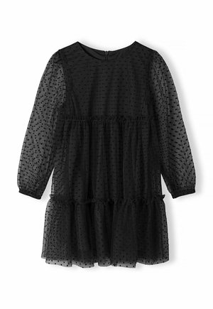 Robe noire à pois blancs en tissu léger et transparent. Elle présente des manches longues, une taille froncée et une jupe à volants.