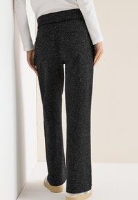 Pantaloni neri a gamba larga con trama testurizzata, vita alta e senza tasche visibili, abbinati a calzature di colore chiaro.