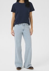 Laivinsininen puuvillapaita yhdistettynä vaaleansinisiin, leveälahkeisiin farkkuihin. Asussa on rento istuvuus ja hienovaraiset ompeludetaljit.