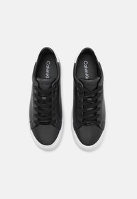 Baskets en cuir noir avec bout arrondi, semelle en caoutchouc blanche et lacets noirs. Présente le logo Calvin Klein sur la languette et le côté. Design simple.