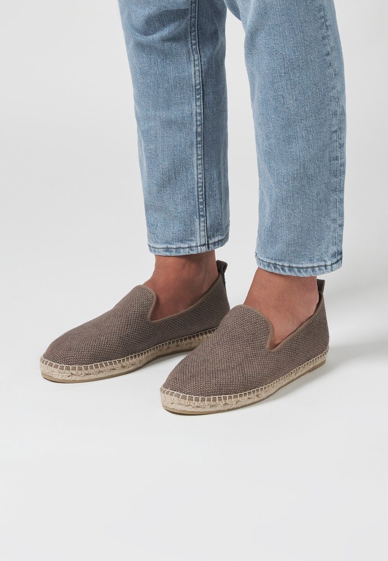 Chaussures slip-on tissées marron avec une semelle en espadrille plate et des détails en corde beige clair le long de la base. Design simple et forme de bout arrondi.