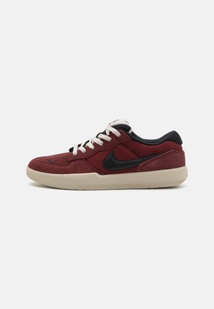 Niski bordowy sneaker z czarnym logo Nike, białymi sznurowadłami, czarnym wyściełanym kołnierzem i beżową podeszwą na białym tle.