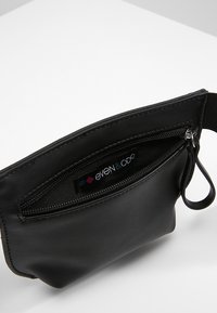 Musta synteettinen pussukka vetoketjulla, jossa kangasmerkki ja kiinnityslenkki. Sileä pinta, kompakti suorakulmainen muoto.