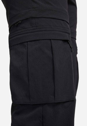Black cargo pants featuring a pleated design, multiple pockets, and drawstring accents. Made from a durable, textured fabric.