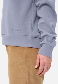 Hellblaues Sweatshirt mit gerippten Bündchen und Saum, das dezent mit einem VAUDE-Logo versehen ist. Das Material wirkt weich und strukturiert.