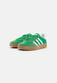 Zelené semišové tenisky s bílými pruhy a akcenty, s gumovou podrážkou a strukturovaným designem svršku. Značka: Adidas Gazelle.
