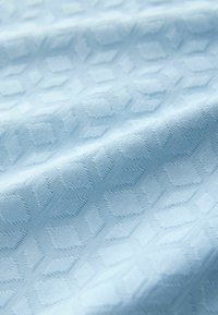 Material albastru deschis cu un model texturat în formă de diamant ridicat și pliuri subtile care creează umbre moi.