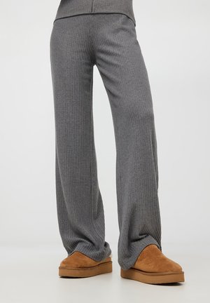 Pantaloni larghi a coste grigi in maglia con una texture liscia, abbinati a pantofole in suede color beige con suola piatta e punta arrotondata.