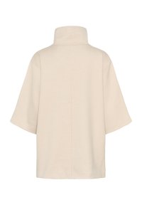 Lyse beige oversized top med højt krave, korte brede ærmer og et simpelt, rent design med en glat tekstur.
