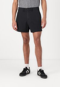 Shorts en coton noir avec une coupe droite, fermeture à bouton et poches latérales. Portés avec des baskets noires aux accents blancs.