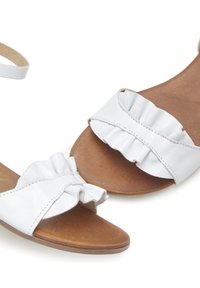 White leather sandals featuring a ruffled strap design and a brown leather footbed. Open-toe style with an adjustable ankle strap.