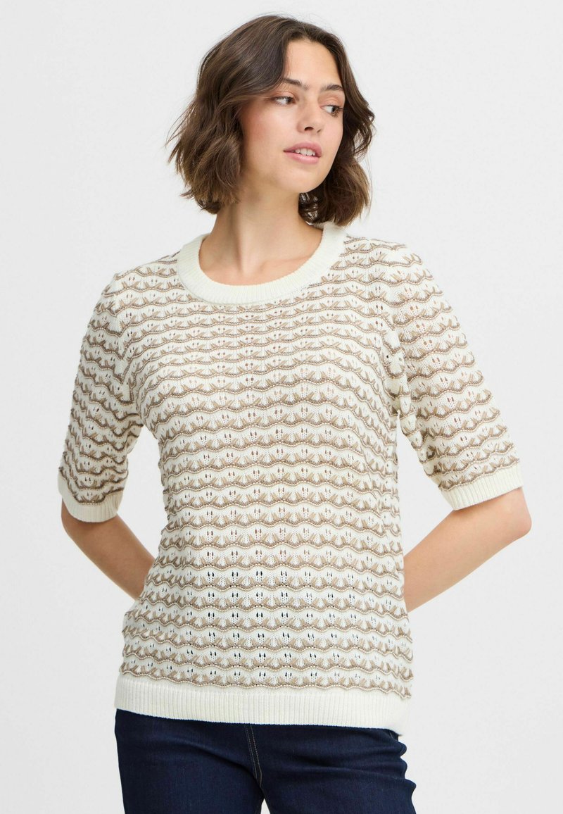 Suéter de manga corta en crema y beige con un patrón de olas texturizadas, cuello y puños de canalé. Se combina con denim oscuro.