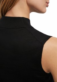 Zwarte mouwloze top met een hoge kraag, gemaakt van een textuur gebreid stof en gladde schoudernaad. Het ontwerp is minimalistisch en aansluitend.