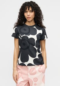 Μπλουζάκι με κοντό μανίκι σε ασπρόμαυρο λουλουδάτο σχέδιο, κατασκευασμένο από μαλακό ύφασμα με στρογγυλή λαιμόκοψη, συνδυασμένο με ανοιχτοροζ παντελόνι με σχέδια.
