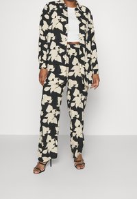 Set di camicia e pantaloni con stampa floreale nera e crema, caratterizzato da una vestibilità ampia, tessuto leggero, chiusura con bottoni e tasche laterali.