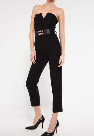 Mustat olkaimeton haalaripuku, jossa on V-kaula-aukko, tiukka vartalonmuotoilu ja leveät, lyhennetyt housut. Varustettu teksturoidulla mustalla vyöllä, jossa on kultasävyisiä yksityiskohtia.