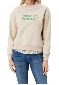 Sweat-shirt beige avec inscription verte « positive MINDSET », col rond, épaules tombantes, et un ourlet de chemise à motif floral visible en dessous.
