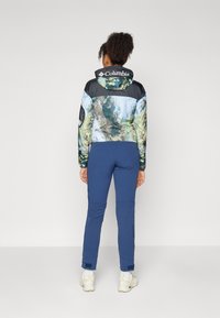 Columbia jakna ima plavi i zeleni uzorak prirode s crnim gornjim dijelom, u kombinaciji s prilagođenim plavim hlačama. Glatka tekstura, džepovi na patentni zatvarač.