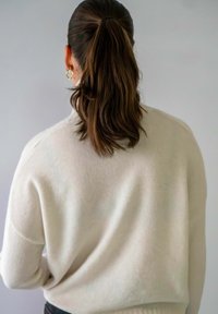 Chunky crème trui met een ontspannen pasvorm, voorzien van een zachte textuur, verlaagde schouders en geribde boorden, gedragen met donkere broeken.