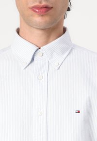Lyseblå stribet skjorte med knapper, der har en klassisk krave og et lille logo broderet på brystet. Glat bomuldsstoffet.