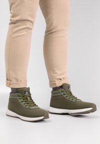 Baskets montantes vertes en tissu texturé, avec une pointe arrondie, une semelle blanche contrastante et un design à lacets verts.