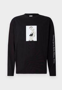 Zwart langemouwen T-shirt met een zwart-witfoto van een vrouw in lingerie op de voorkant en witte tekst op de rechtermouw.