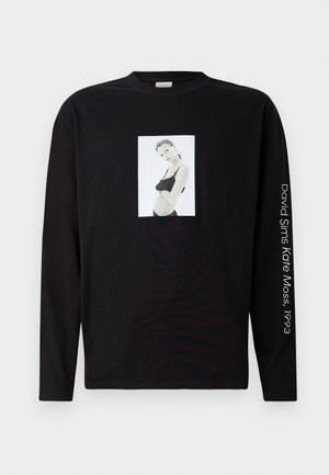 Zwart langemouwen T-shirt met een zwart-witfoto van een vrouw in lingerie op de voorkant en witte tekst op de rechtermouw.