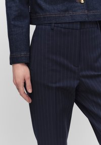 Donkerblauwe denimjacket met contrasterende oranje stiksels, gecombineerd met marineblauwe pinstriped broek met een slim fit en zijzakken.