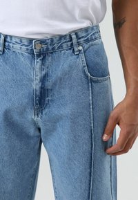 Lichtblauwe spijkerbroek met een klassiek ontwerp, rechte pijpen, voorzakken en een zilveren knoopsluiting in de taille.