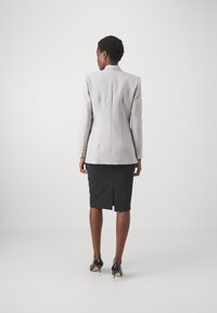 Blazer ajustado de color gris claro con hombros estructurados, costuras traseras y puños abotonados, combinado con una falda lápiz negra con una abertura en la parte trasera.