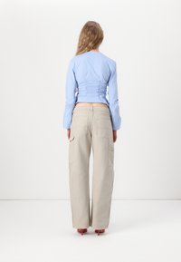 Light blue long-sleeve shirt with gathered back detail, paired with loose beige cargo pants featuring large side pockets. Pink high-heeled shoes visible.