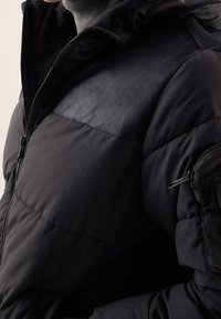 Czarna kurtka puchowa z pikowanym wzorem. Teksturowany materiał na górnej części, kieszenie na zamek oraz wysoki kołnierz.