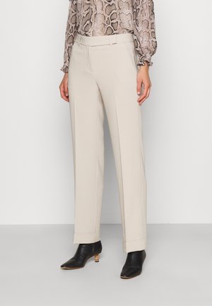 Pantalones beige a medida con puños usados por una persona con botines de tacón negro y una blusa con estampado de serpiente.