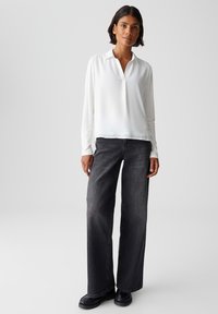 Weiße Bluse mit langen Ärmeln und Kragen, kombiniert mit schwarzen weiten Jeans und schwarzen Schuhen. Glatte Textur, lockere Passform und schlichtes Design.