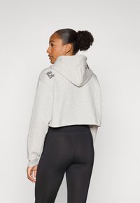 Felpa grigia tagliata con cappuccio, con testo nero sulla spalla sinistra. Abbinata a leggings neri a vita alta, che mettono in risalto uno stile aderente.