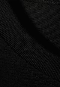 Gros plan sur un tissu noir tricoté montrant un col côtelé et la texture détaillée du vêtement.