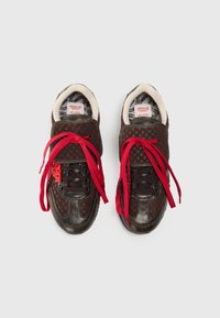 Brown sneakers with a checkered pattern, red laces, and a soft white lining. Features a smooth leather texture and prominent branding.