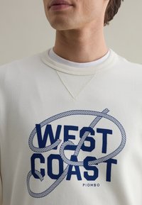 Felpa color crema con stampa blu "WEST COAST" e design a corda. Presenta un collo tondo e un tessuto testurizzato. Vestibilità casual.