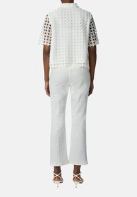 Witte kant top met ruitvormige uitsparingen, korte mouwen en kraag, gecombineerd met witte flared broek en sandaaltjes met straps.