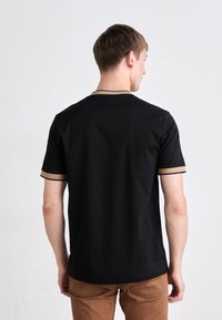 Schwarzes T-Shirt mit kurzen Ärmeln und beigem Rand am Kragen und an den Ärmeln, das eine weiche Textur und eine lockere Passform bietet.