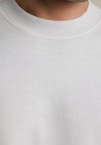 Jasnoszara bawełniana bluza z okrągłym dekoltem, charakteryzująca się gładką teksturą i ściągaczem przy kołnierzu. Zbliżenie pokazuje detale stichingu.