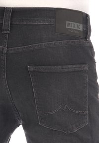 Jeans de mezclilla negros con un bolsillo trasero visible que presenta un diseño de costura distintivo. Incluye una etiqueta de cuero negra con la marca.