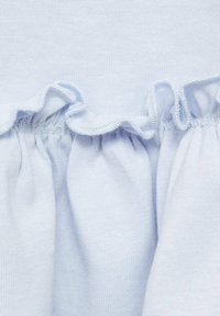 Ljusblått bomullstyg med inslag av rynkade volanger längs sömmen. Texturen är mjuk och slät, med synlig sömnad.