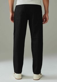 Pantaloni din denim negri, cu croială dreaptă și buzunare pe spate, asortați cu adidași albi cu talpă joasă. Textură netedă, design minimalistic.