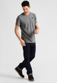 T-shirt gris con cuello redondo, combinada con jeans de mezclilla oscuros. Tela texturizada, logo en el pecho y botas marrones con puños enrollados.