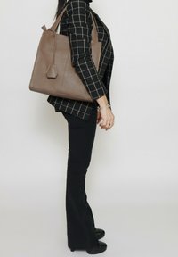 Bruine lederen tote bag met een hexagonaal label, voorzien van een gestructureerd ontwerp, zachte textuur en dubbele schouderbanden.