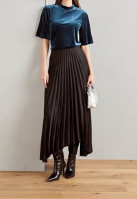 Sametový teal top s krátkými rukávy, spárovaný s černou plisovanou midi sukní a černými špičatými vysokými botami. Doplněk: malá lesklá stříbrná kabelka.